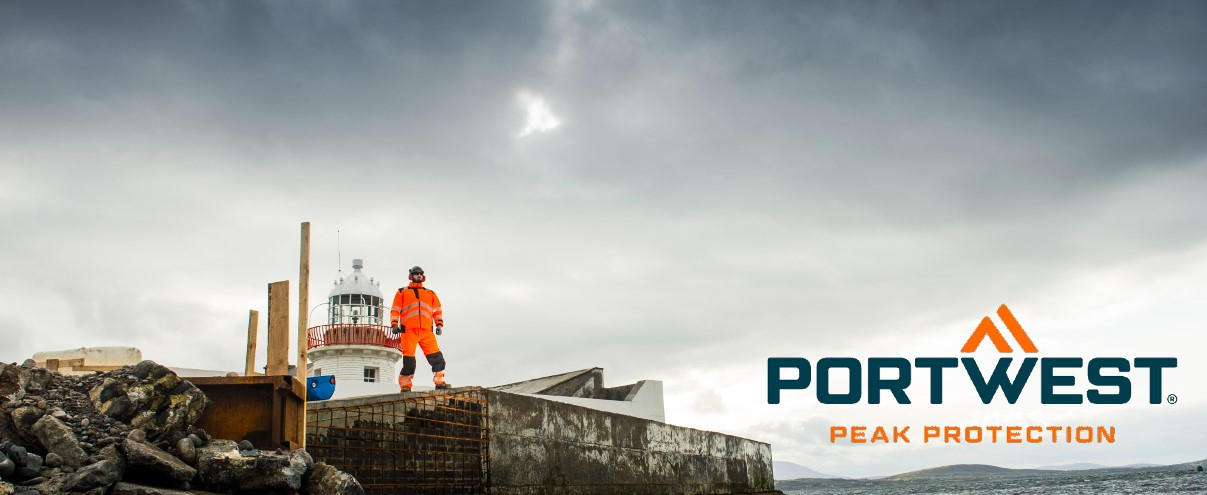 Un lavoratore che indossa indumenti arancioni ad alta visibilità si trova su un cantiere roccioso accanto a un faro, con il logo Portwest e lo slogan "Peak Protection" nella foto.