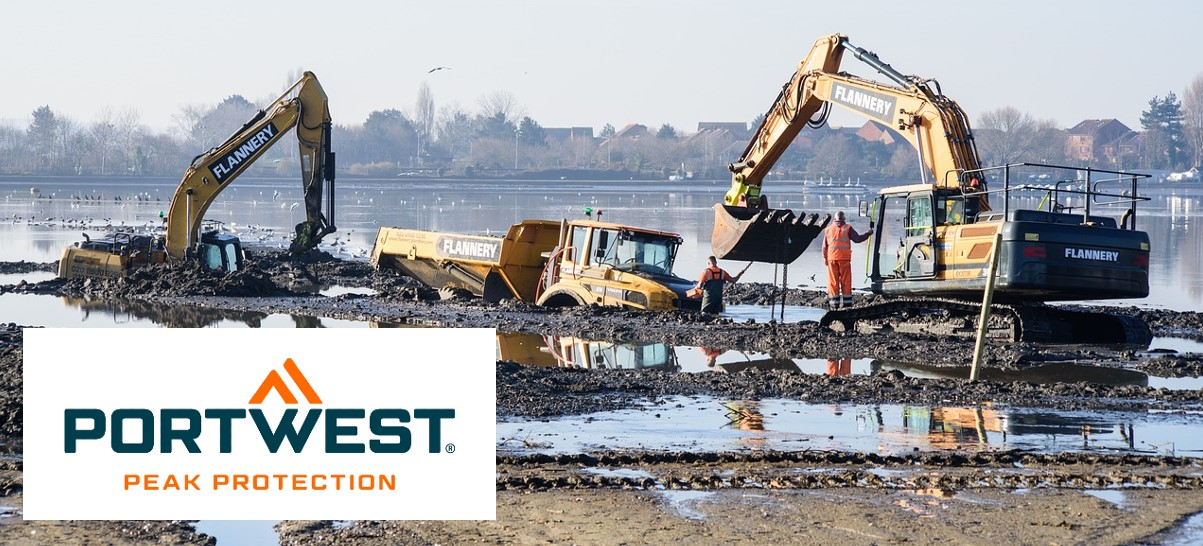 Scena di cantiere con escavatori e macchine di grandi dimensioni. Ci sono pozzanghere e fango per terra, il cielo è azzurro e all'orizzonte si vedono alcune case e alberi.