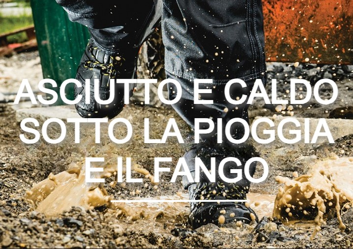 Operaio in pantaloni e stivali antipioggia che cammina in una pozzanghera. Schizzi di fango e sullo sfondo si vede un cantiere edile. C'è un collegamento alle nostre scarpe impermeabili.